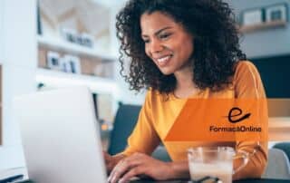 Woman with curly hair wearing an orange top types on a laptop in a bright home office; FormaciónOnline logo visible on her chest.