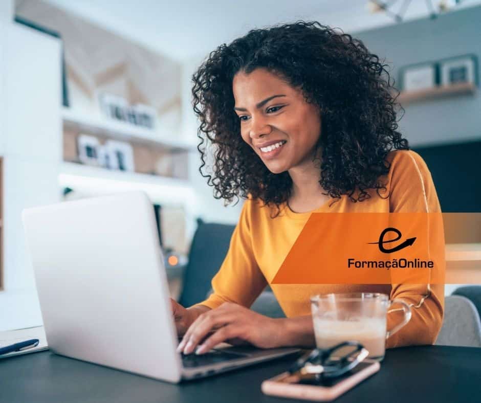 Woman with curly hair wearing an orange top types on a laptop in a bright home office; FormaciónOnline logo visible on her chest.