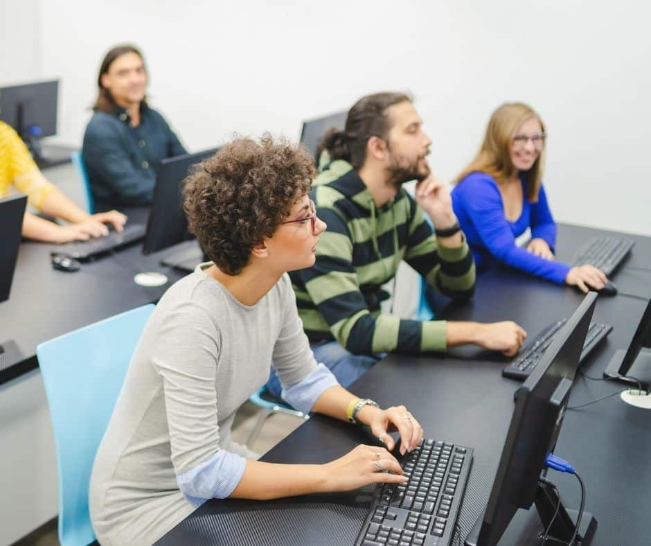 Group of students in a computer lab working at desktop PCs, looking toward the front of the room.