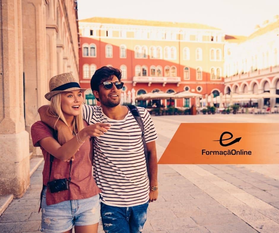Couple in casual outfits with a camera, pointing ahead in a sunny plaza with colorful buildings and an orange FormacaoOnline banner to the right.