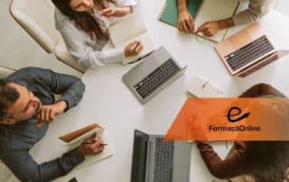 Overhead view of four people around a white table with laptops and notebooks; an orange 'e FormaçaoOnline' banner sits on the right.